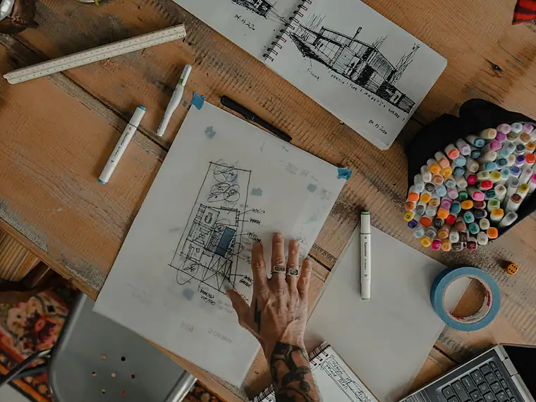 Mãos sobre uma prancha de estudo, com compasso e croquis